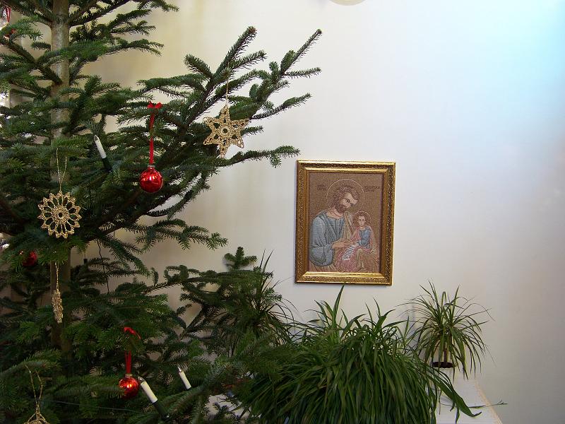 09.JPG - Über der Kredenz, auf der die Opfergaben Wein, Wasser und Brot bereitgestellt werden, hängt das Bild des Nährvaters St. Josef mit dem Jesuskind in goldenem Rahmen. Die Bäume wurden mit Glaskugeln und gehäkelten Sternen geschmückt, die von den Landfrauen gebastelt wurden.